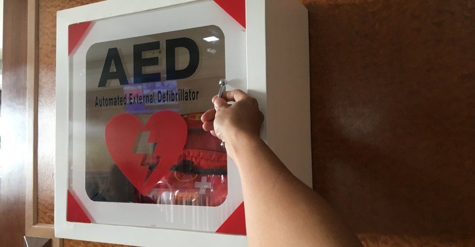 Hand opening a wall-mounted AED cabinet